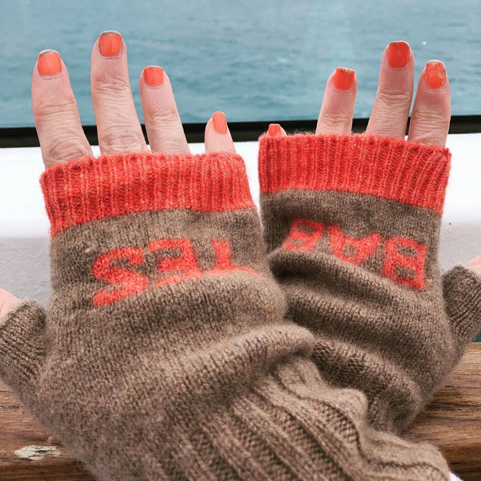 Packing for a Norwegian Fjords Cruise in May | Hands clad in brown and orange mittens with Yes Bab printed on them